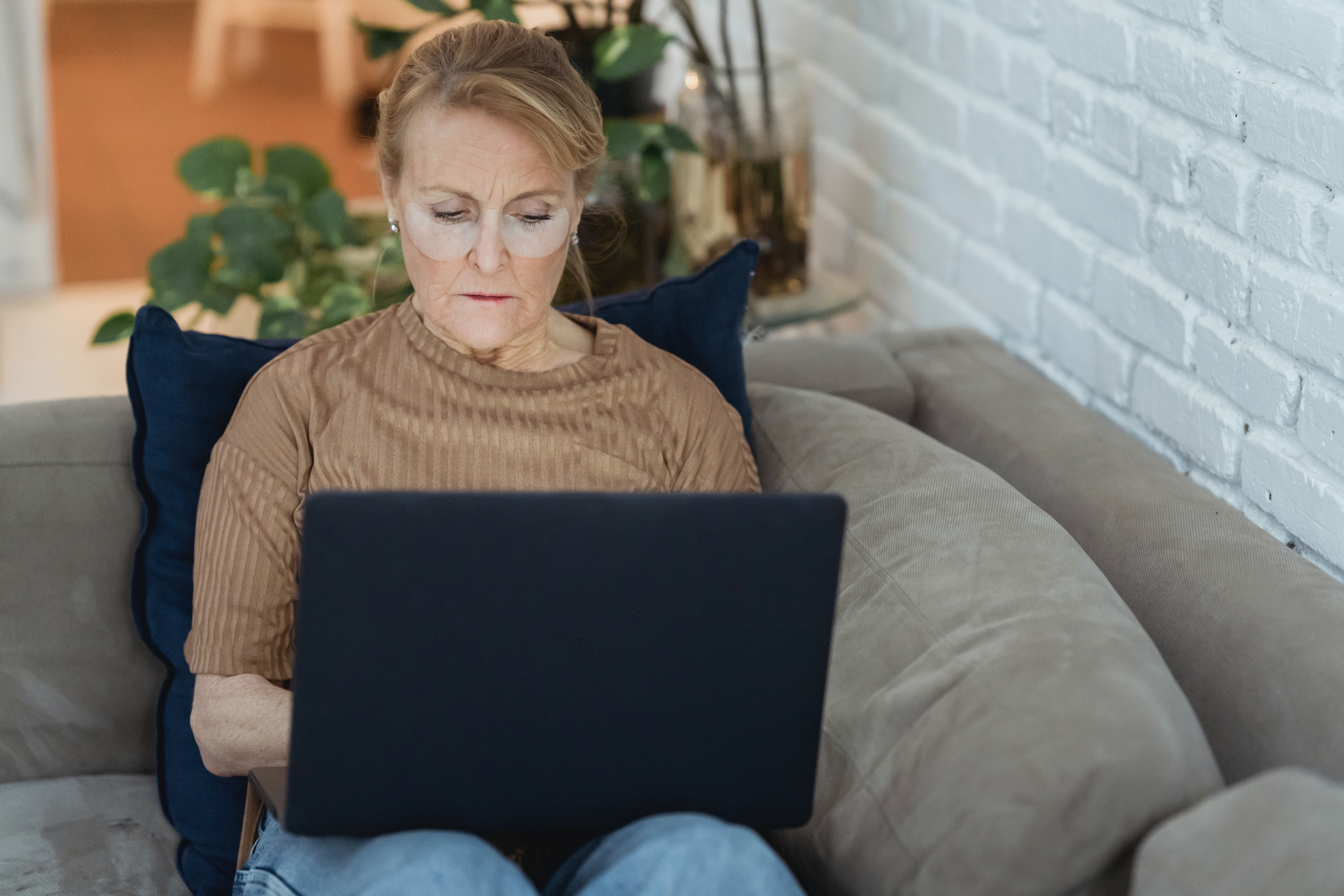 Ältere Drau sitzt auf der Couch und einen Laptop auf dem Schoß