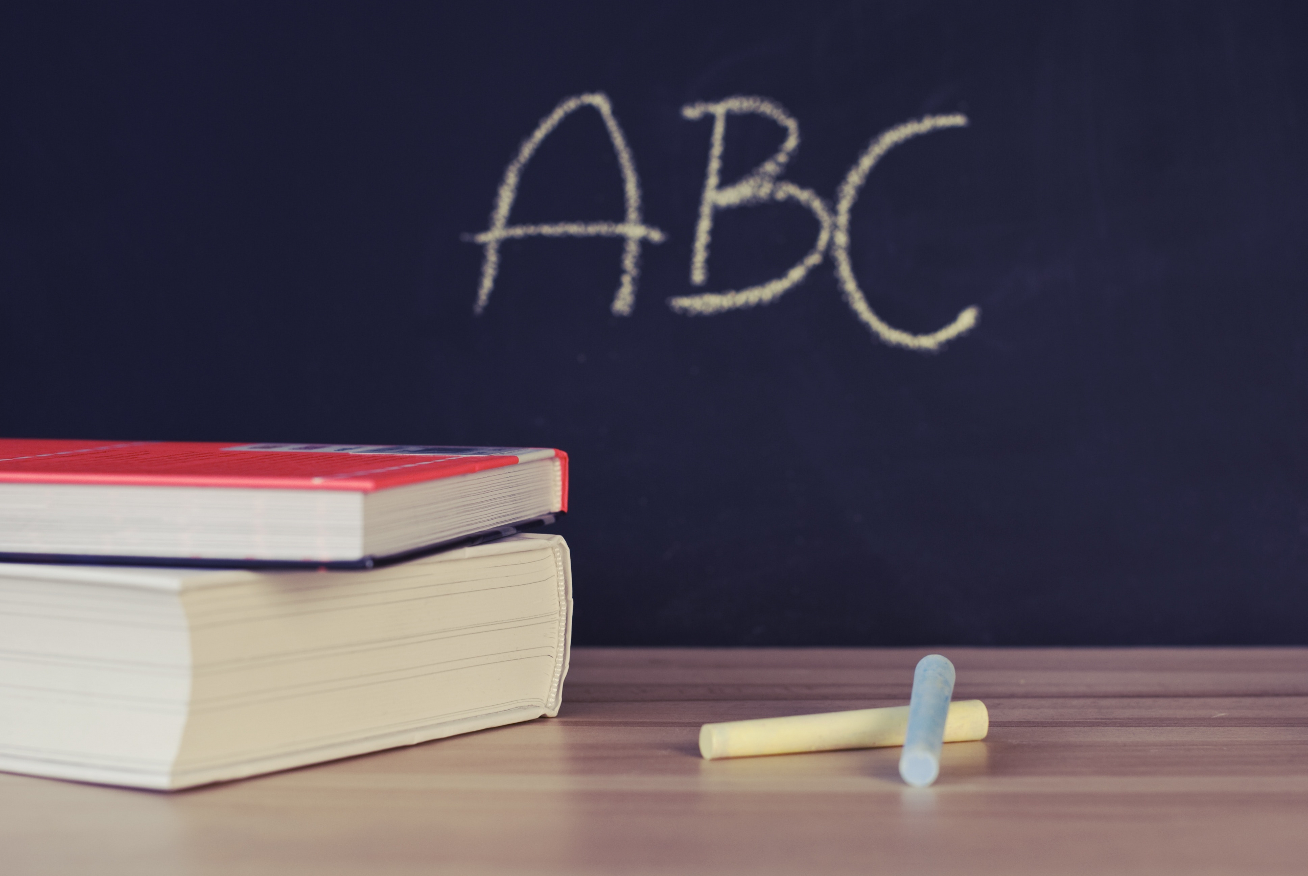 Schultafel auf der ABC steht. Davor ein Tisch mit Kreide und Büchern drauf